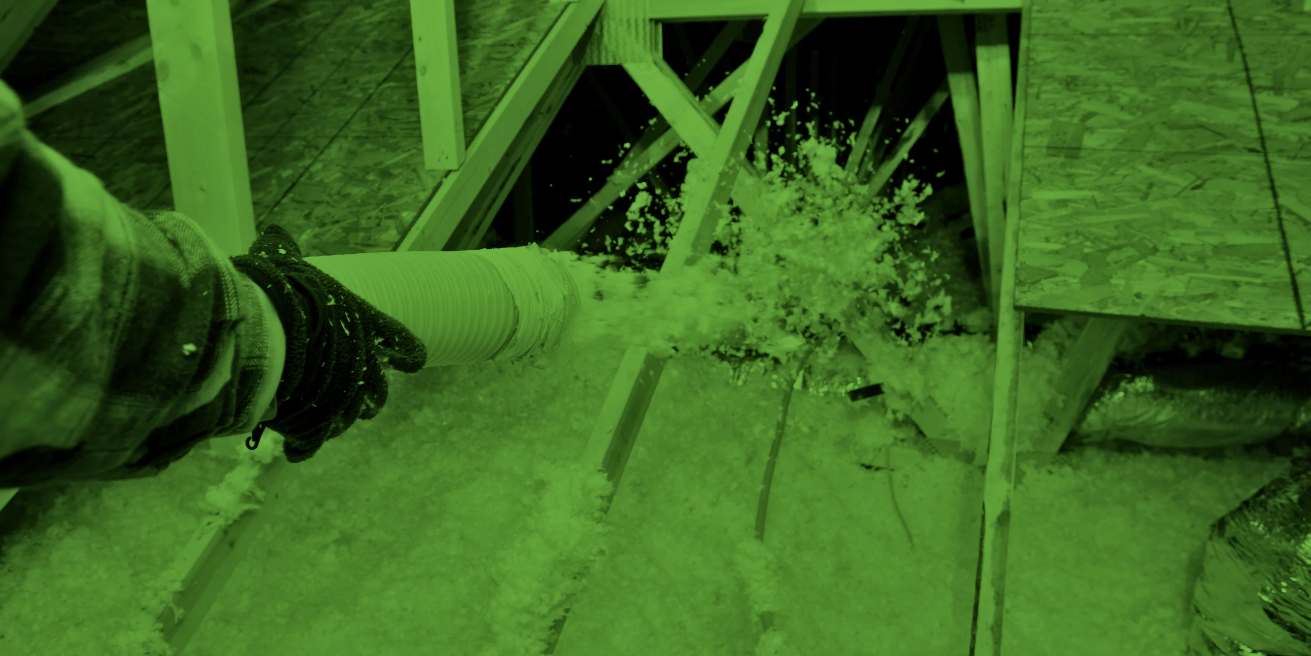 a hand holding a tube spraying fiberglass insulation in the attic